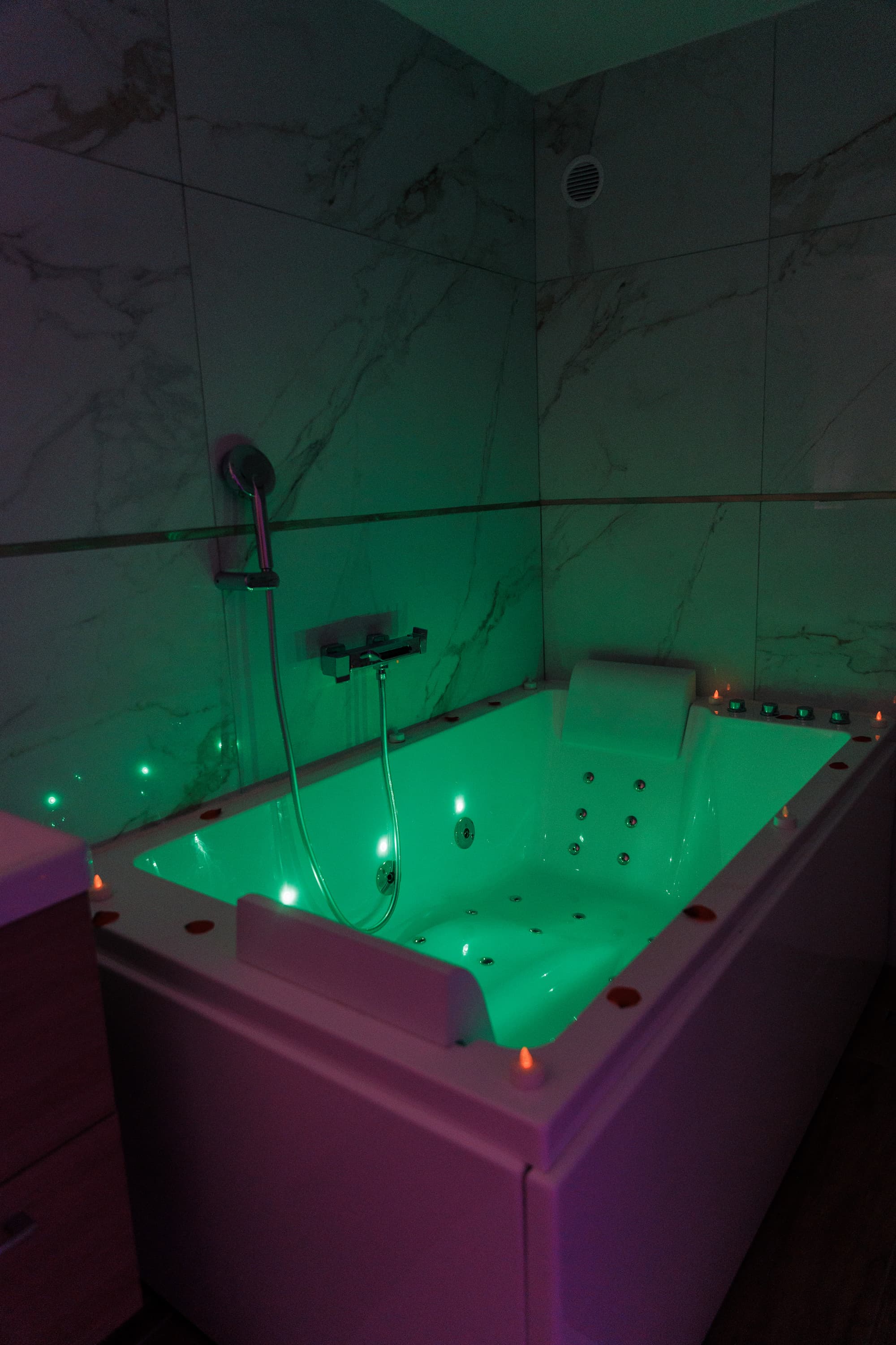 Jacuzzi privatif éclairé d'une lumière douce, habillé de marbre et de bougies